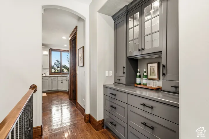 Built-in cabinetry with glass-front uppers, wood-finish flooring, and arched hallway entrance