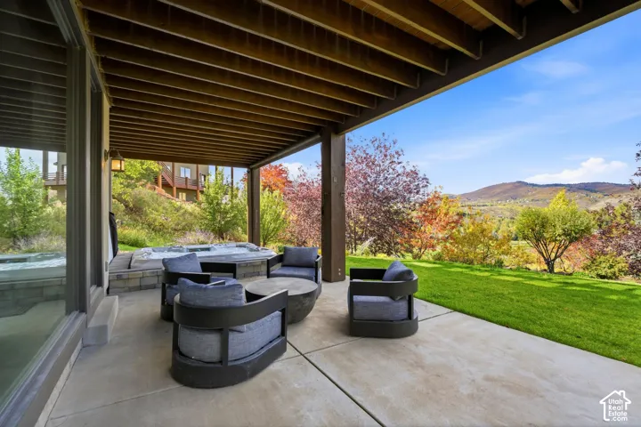 Covered concrete patio with an integrated hot tub, surrounded by a stone-faced retaining wall and a manicured lawn