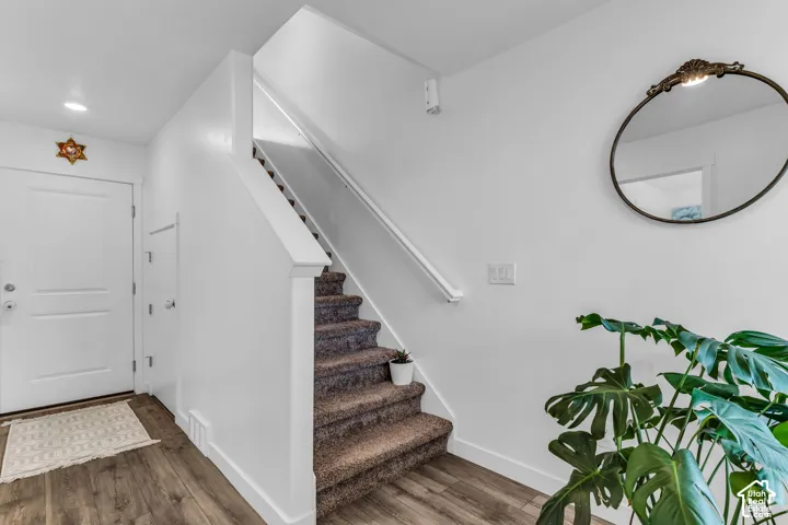 Wood-finish flooring, white painted walls, recessed lighting, and carpeted stairs