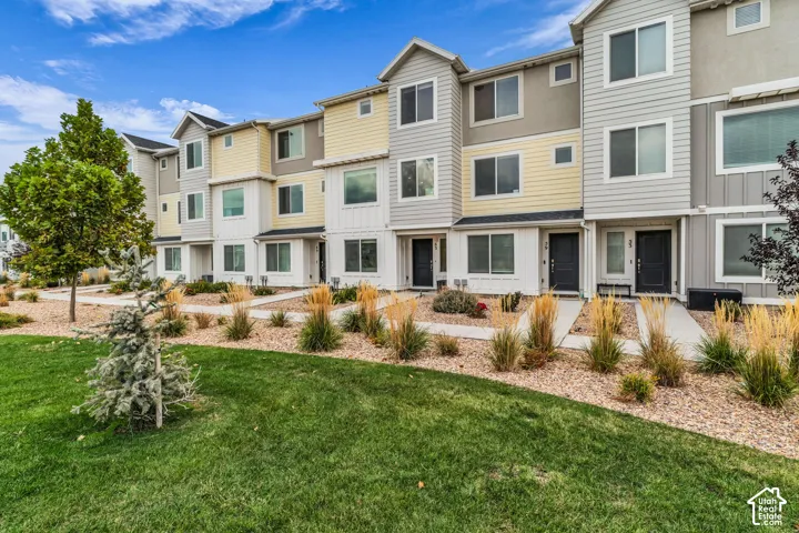 Contemporary townhome facade with mixed material siding, multiple windows, and a landscaped front yard with grass and decorative plantings