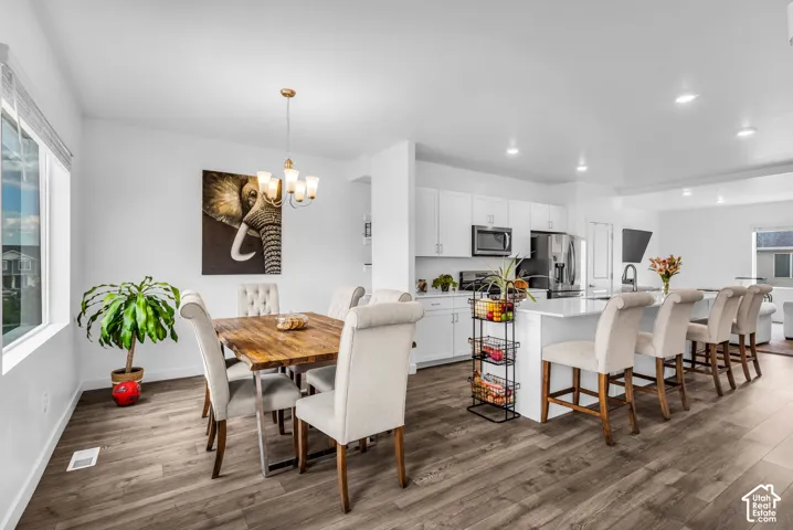 Open-concept living space featuring wood-finish flooring, a dining area with a chandelier, and a kitchen with white cabinetry