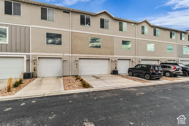 Townhome exterior featuring stucco and vertical siding, individual garage doors, dedicated driveways, and exterior light fixtures