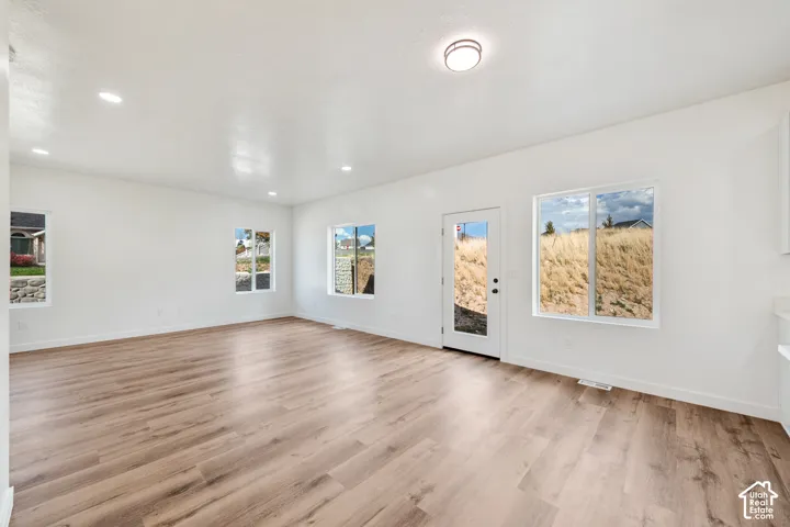 Recessed lighting, wood-finish flooring, multiple windows, white walls, and a glass-paneled exterior door