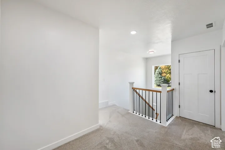 Carpeted hallway with a wood and wrought iron staircase railing, recessed lighting, and a white paneled door