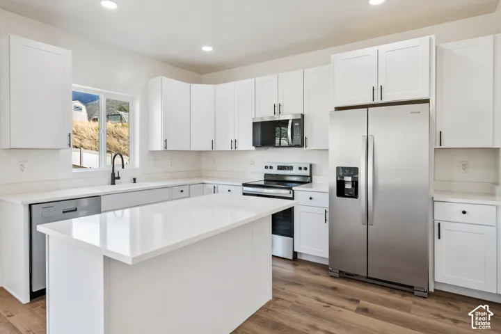 Kitchen featuring white shaker cabinetry, stainless steel appliances, wood-finish flooring, a center island with a solid surface countertop, and a farmhouse-style sink