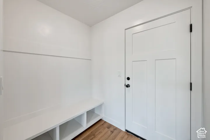 Built-in bench with cubby storage, white interior door with matte black hardware, wood-finish flooring, and white walls