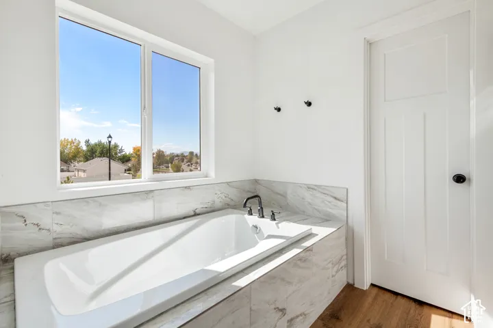 Built-in soaking tub with a tiled surround, large window, and matte black fixtures