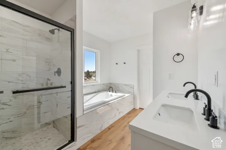 Dual vanity with matte black fixtures, built-in soaking tub, walk-in shower with glass enclosure, wood-finish flooring, and a window for natural light