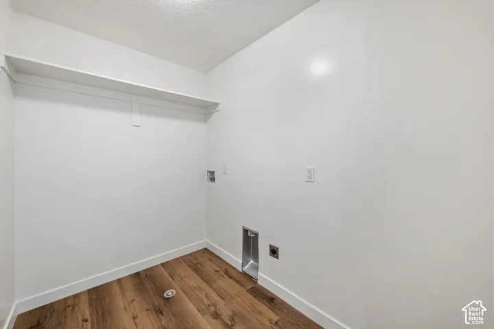 Wood-finish flooring with white baseboards, integrated wall shelving, and utility hookups