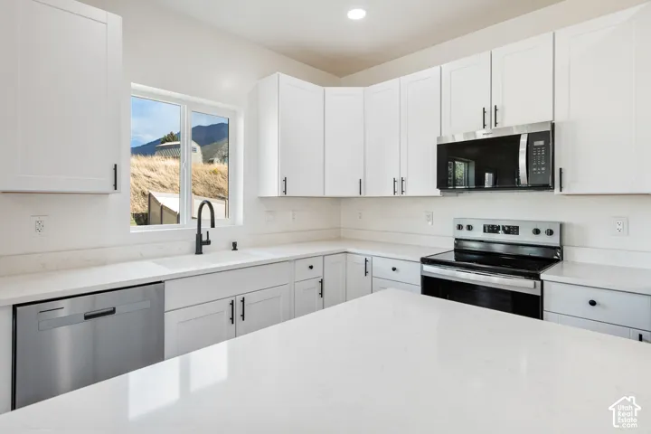 White shaker-style cabinetry, stainless steel appliances, white countertops, and a matte black gooseneck faucet