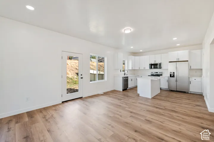 Spacious open-concept living area featuring wood-finish flooring, recessed lighting, and a white kitchen with stainless steel appliances