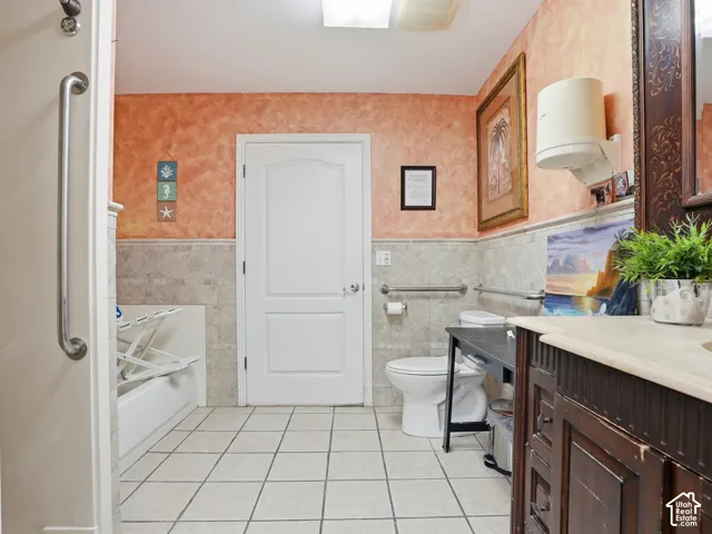 Ceramic tile flooring, textured wall finish, full-height wall tile, and a wooden vanity with a stone countertop
