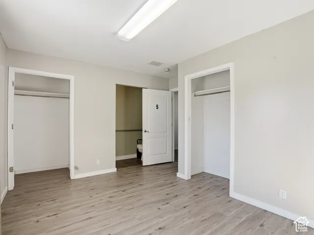Room featuring wood-finish flooring, two open closet spaces with hanging rods, and a white interior door
