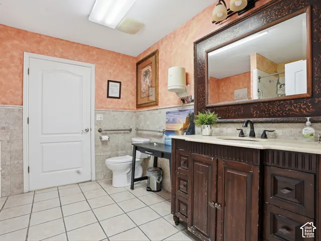 Tiled flooring with half-wall tile surround, a dark wood vanity with counter, and a large framed mirror
