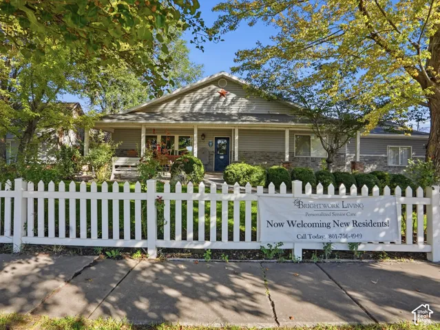 Gable roofline, covered front porch, light gray siding, stone veneer accents, and white picket fence