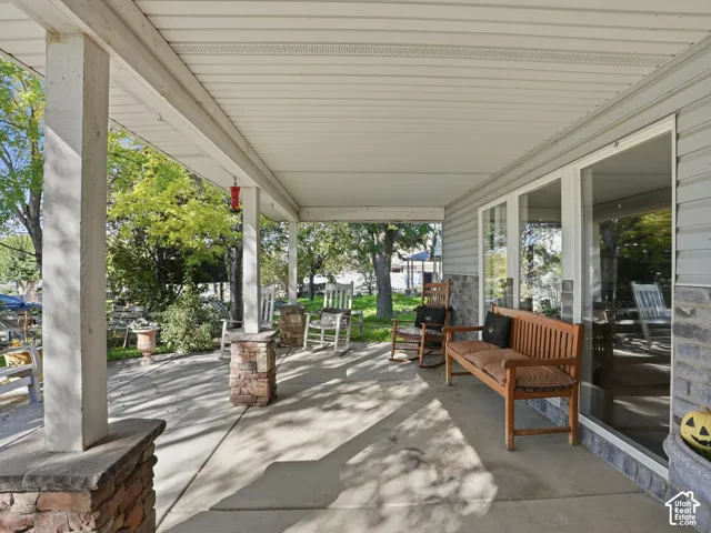 Covered porch with concrete flooring, stone-clad pillars, and sliding glass doors