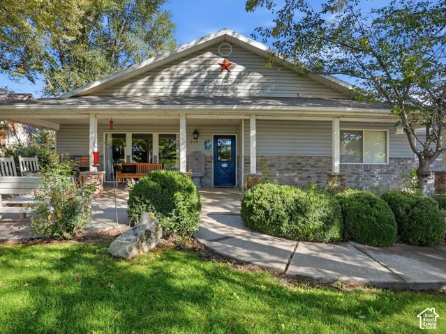 Covered front porch with stone and siding facade, concrete walkway, and mature landscaping