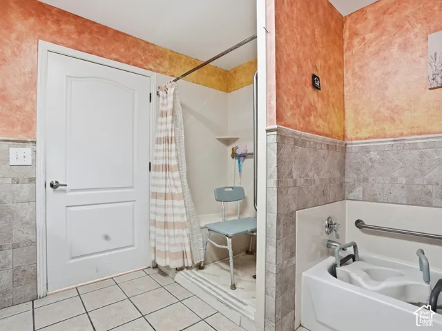 Tiled flooring and wainscoting, walk-in shower, built-in grab bars, and a white soaking tub