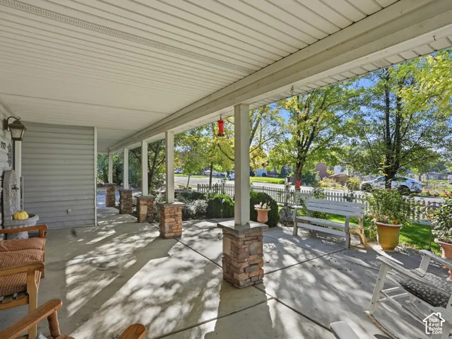Covered porch featuring a concrete surface, stone-clad columns, and a white picket fence