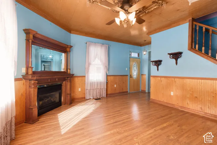 Hardwood-finish flooring, wood paneling, decorative ceiling fan, and ornate fireplace with a built-in mirror