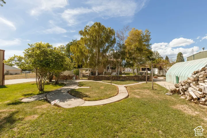 Expansive lawn featuring concrete pathways, mature trees, and a distant outbuilding