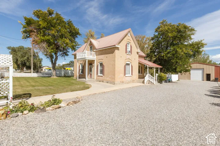 Brick exterior with a metal roof, front porch, second-story balcony, gravel driveway, and a detached metal building