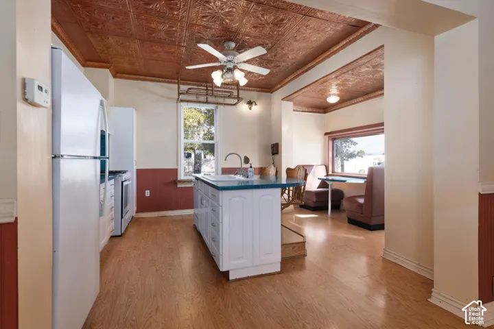 Kitchen featuring a decorative ceiling, wood-finish flooring, central island with sink, and white appliances