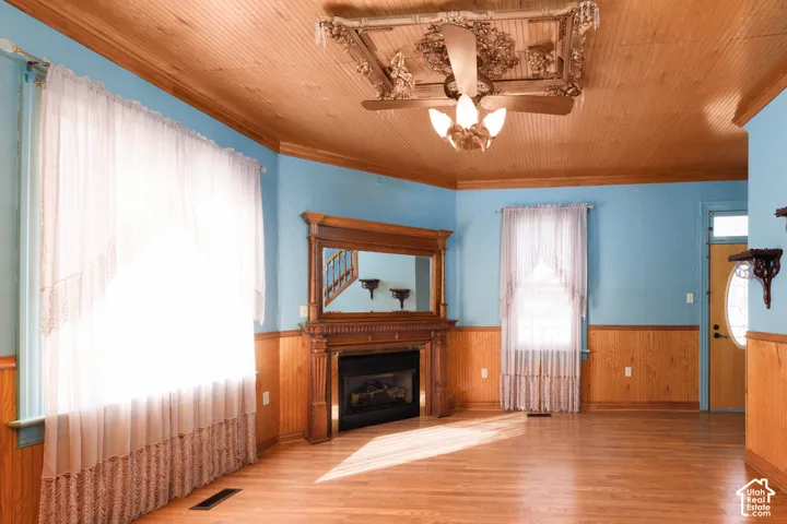 Wood-finish flooring, wood paneling, wood-plank ceiling, ceiling fan with light fixture, and decorative wood mantel with fireplace