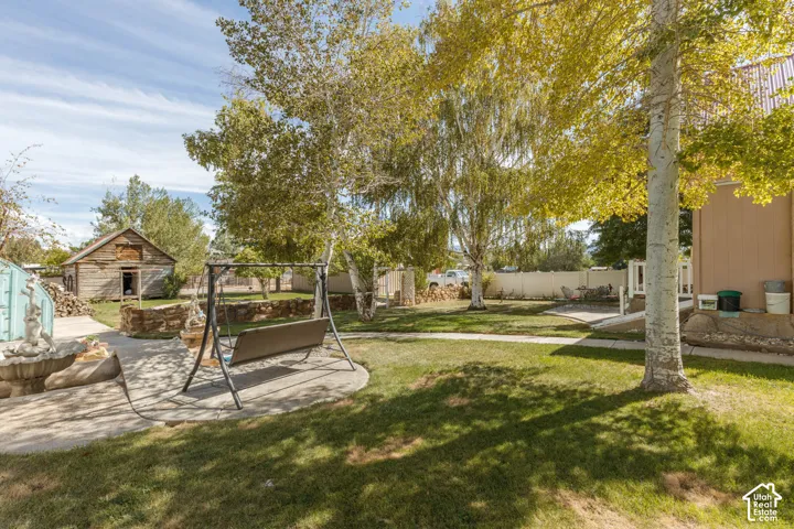 Expansive grassy yard with mature trees, concrete patio, and a rustic wood outbuilding