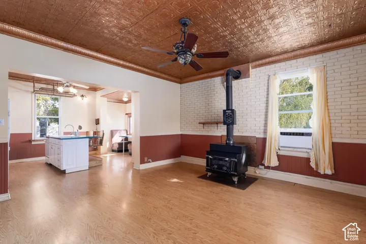 Wood-finish flooring, pressed metal ceiling, exposed brick wall, wood-burning stove, and ceiling fan