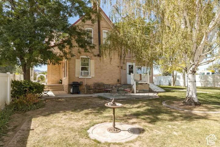 Brick exterior with multiple windows, mature trees, a concrete patio, and a white privacy fence