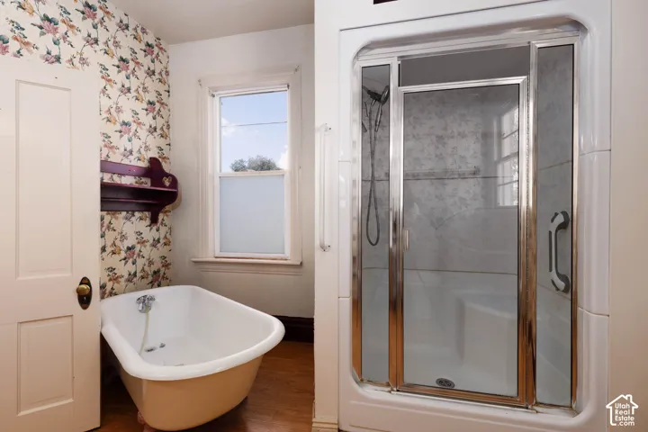 Freestanding clawfoot tub, separate shower enclosure with sliding glass doors, white window frame, wood-finish flooring, and a built-in wall shelf