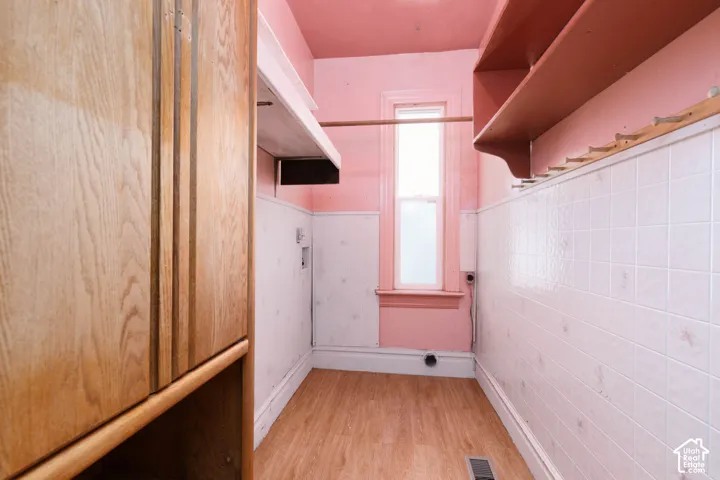 Wood-finish flooring, built-in wooden cabinetry, white wall tiling, single window, and wall-mounted shelving