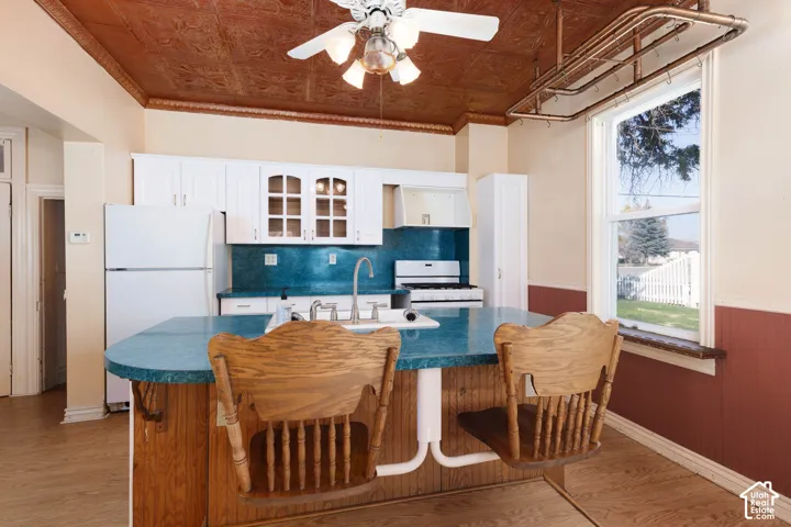 Kitchen featuring a pressed tin ceiling, wood-finish flooring, white cabinetry, a central island with a blue countertop, and a window with a copper-finish pot rack