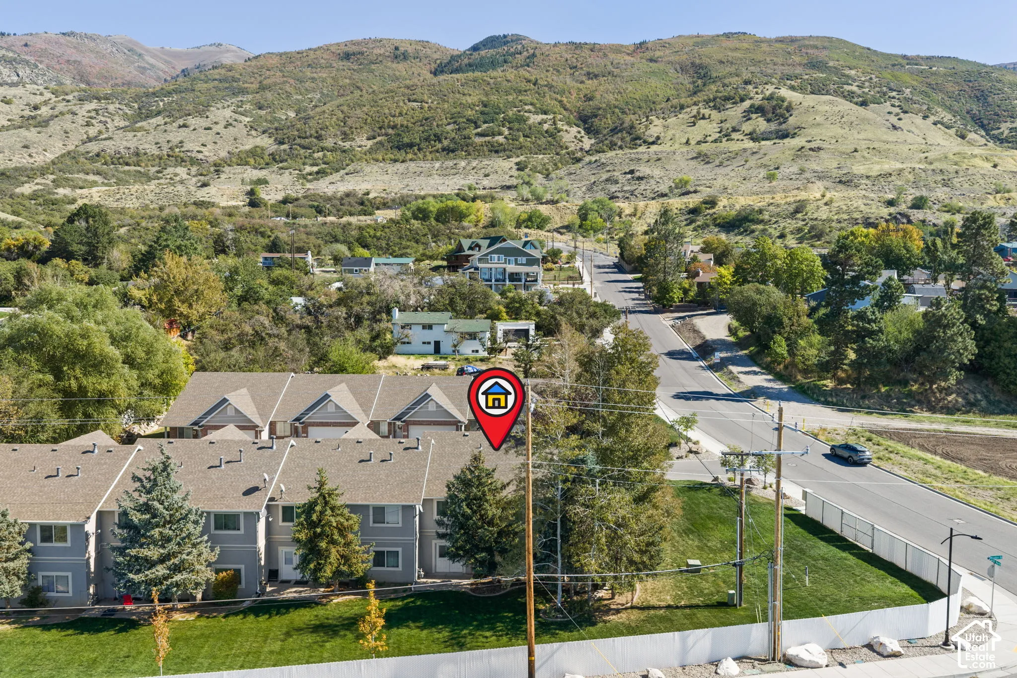 Townhome community nestled in a rolling hillside setting, featuring contemporary architectural design with peaked rooflines, manicured landscaping with mature trees, and a gated entry