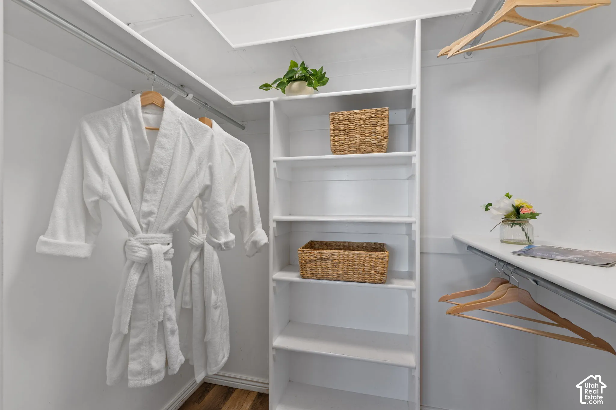 White custom closet system with hanging rods, adjustable shelving, and wood-finish flooring