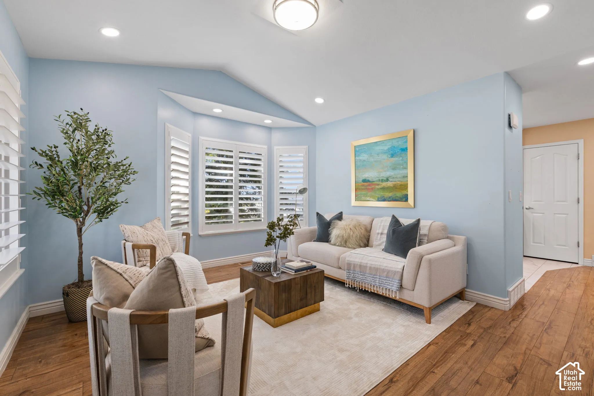 Light-filled sitting room featuring soft blue walls, recessed ceiling lighting, and wood-finish flooring throughout