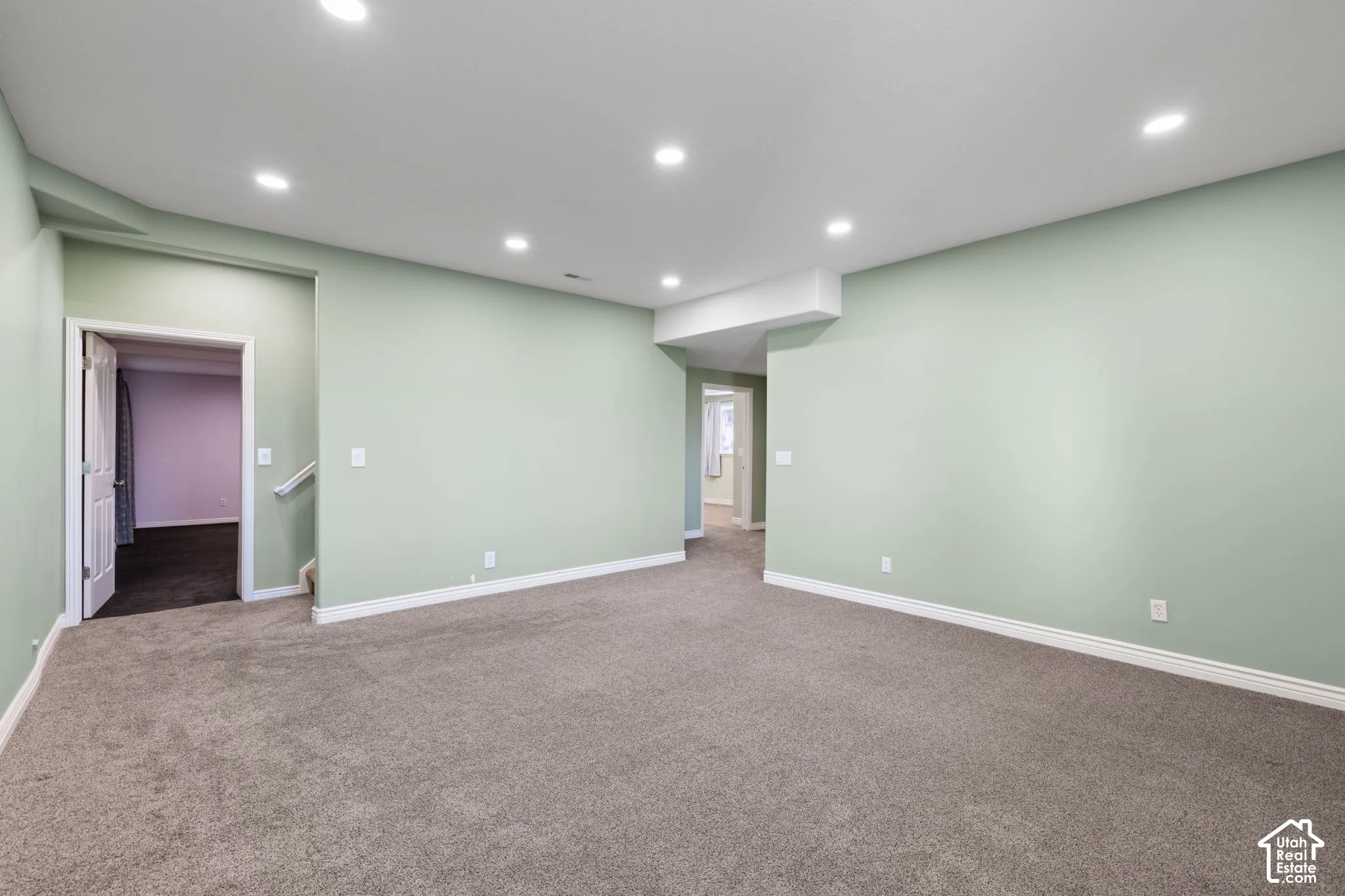 Recessed lighting illuminates the carpeted flooring and light green walls