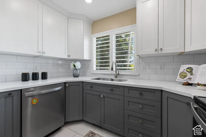 Modern kitchen featuring a two-tone cabinetry design with white upper cabinets and charcoal lower cabinets, stainless steel appliances, subway tile backsplash, quartz countertops, and a corner sink with shuttered windows providing natural light