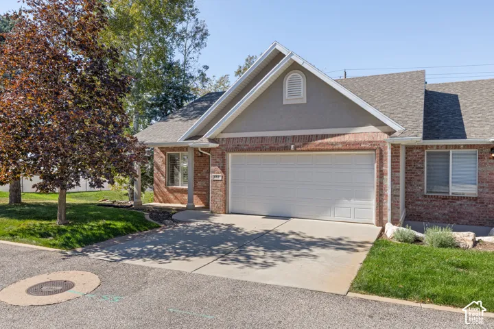 Brick exterior with an attached garage, paved driveway, and mature landscaping
