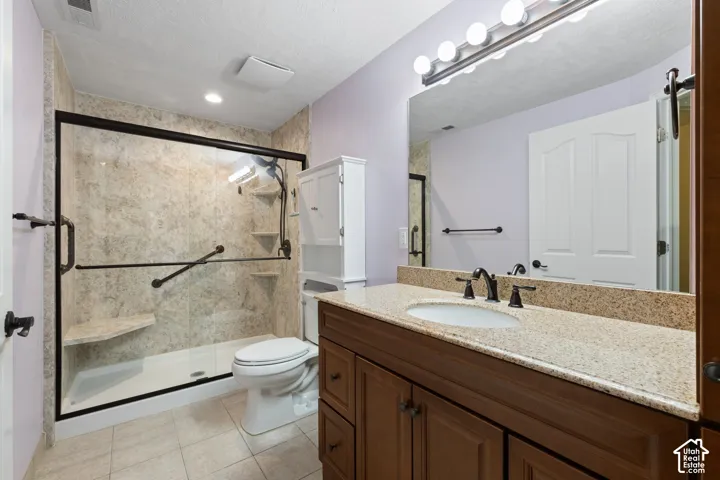 Walk-in shower with grab bars and built-in bench, wood-finish vanity with granite countertop, large vanity mirror, and tile flooring