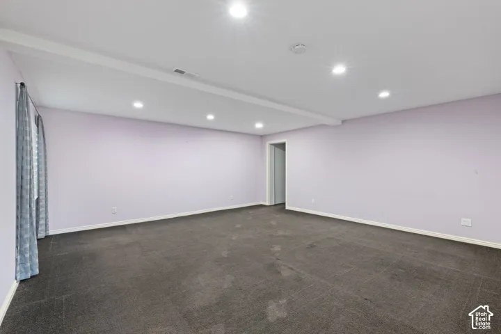 Expansive room with dark carpeting, recessed lighting, and a window with curtain rod