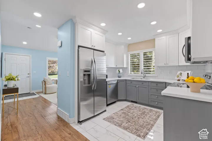 Modern kitchen featuring stainless steel side-by-side refrigerator, white cabinetry with gray lower cabinets, white subway tile backsplash, recessed ceiling lighting, and wood-finish flooring throughout the open layout