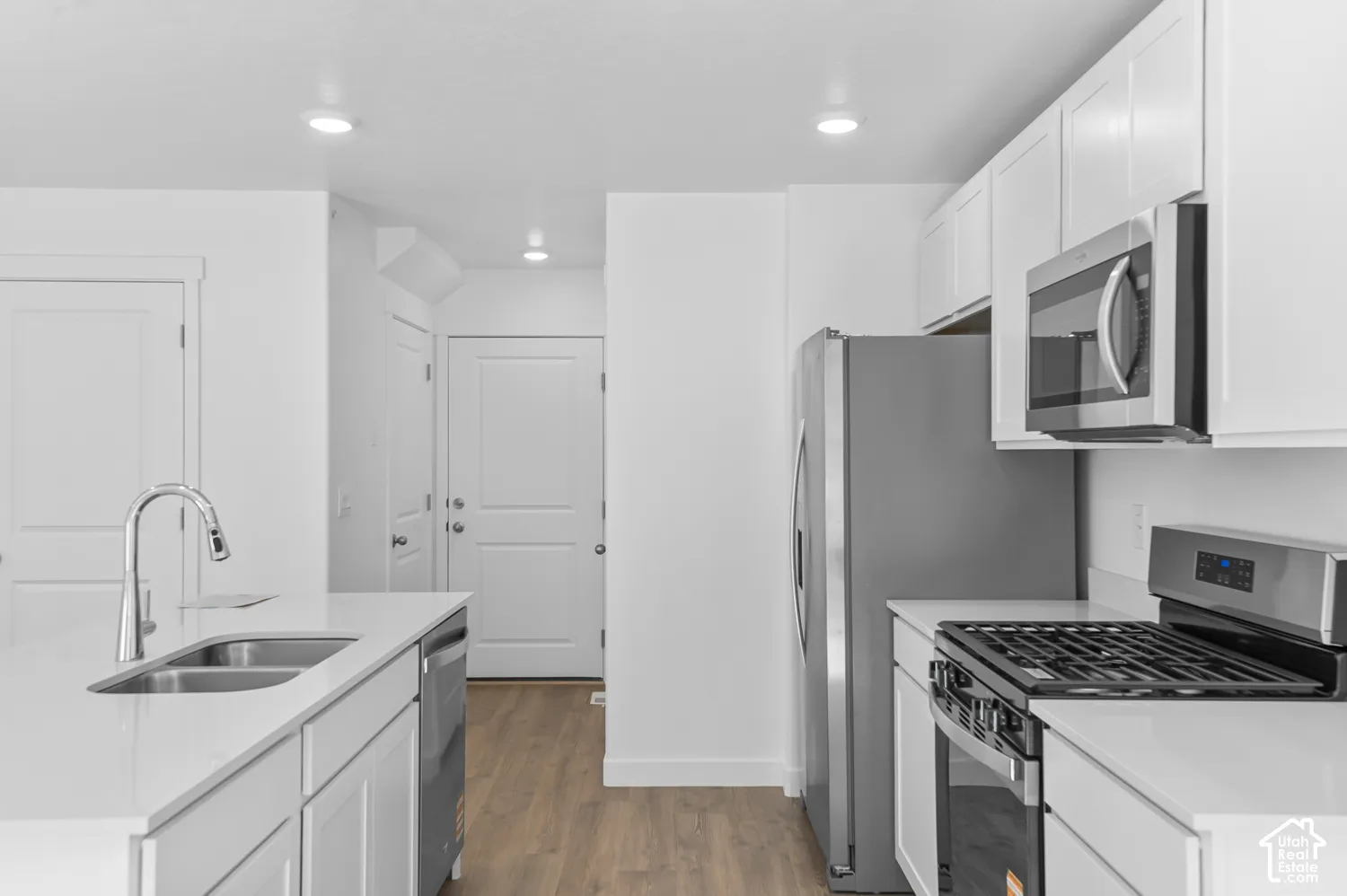 Modern kitchen featuring white cabinetry, light-toned countertops, stainless steel appliances, and wood-finish flooring