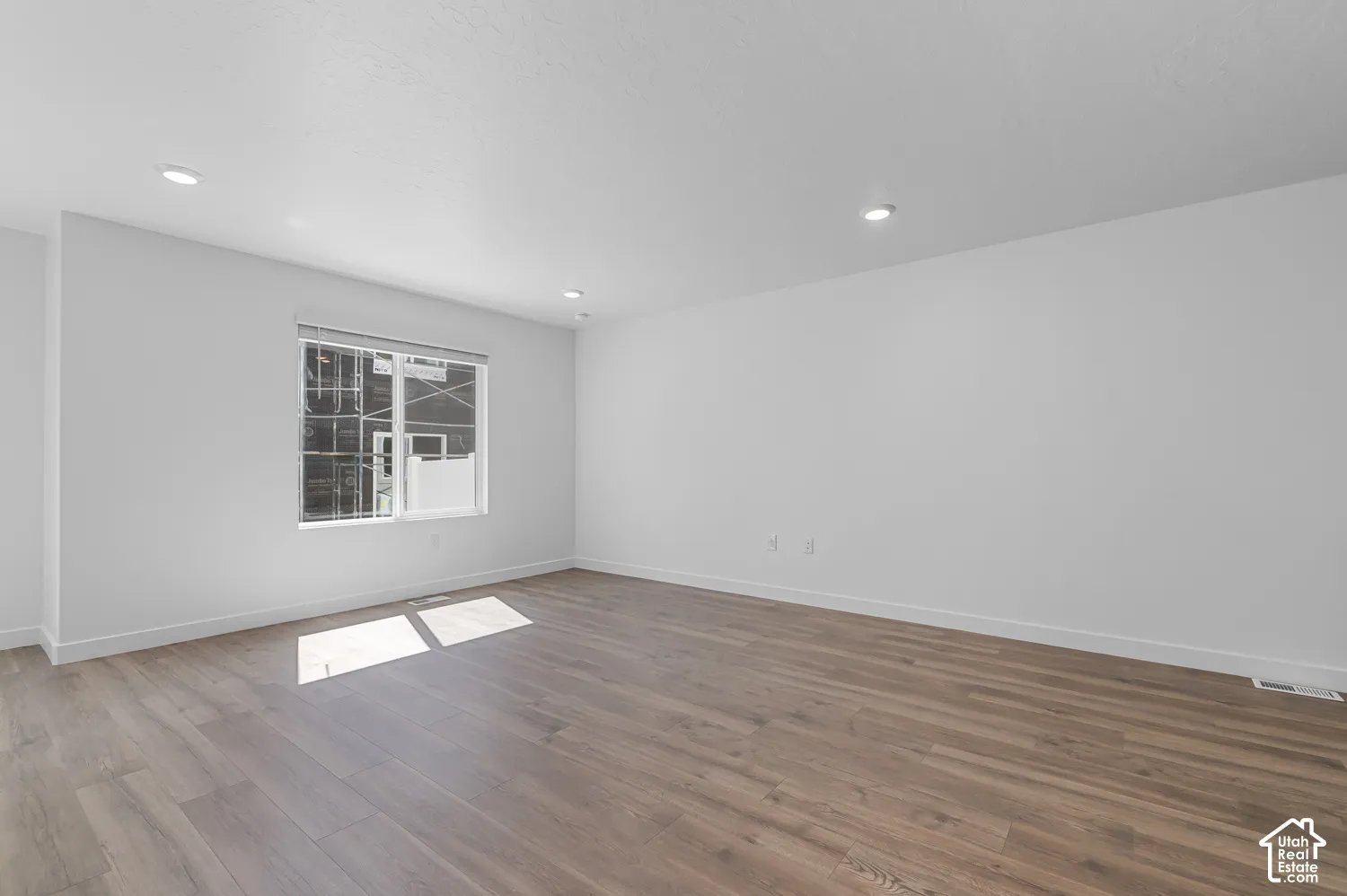 Bright, open room featuring gleaming wood-finish flooring, recessed ceiling lighting, and large windows allowing abundant natural light