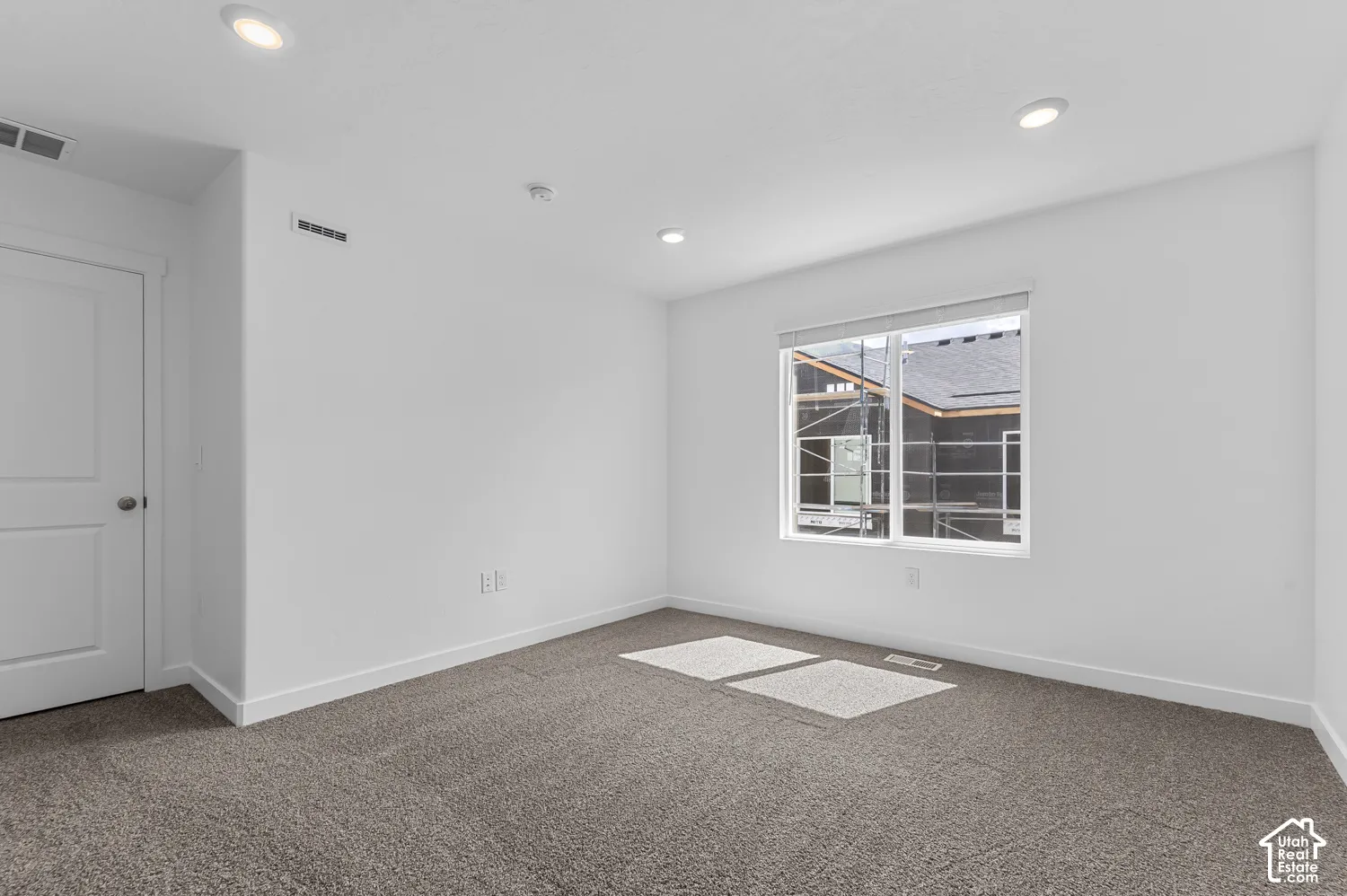 Recessed ceiling lighting, white interior door, light gray carpet, white walls, and a window with blinds