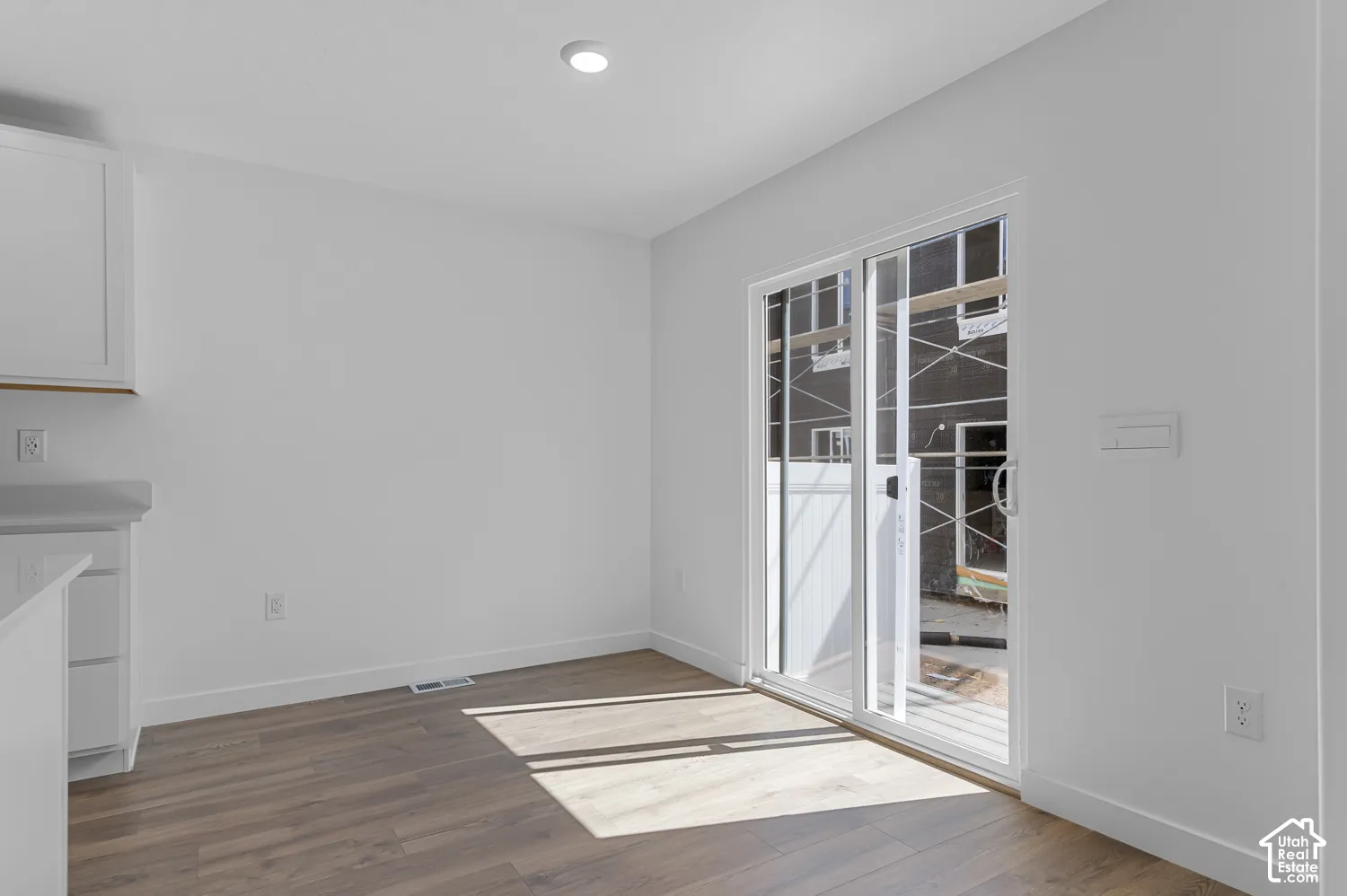 Wood-finish flooring, recessed ceiling lighting, white cabinetry, and sliding glass door