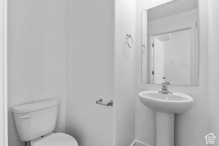 Pedestal sink with chrome faucet, wall-mounted mirror, and white toilet