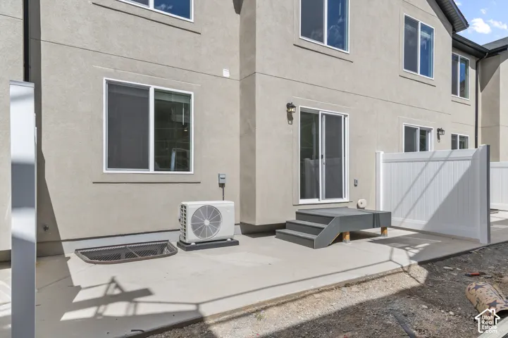 Stucco exterior with multiple windows, sliding glass door, patio with steps, and a white privacy fence