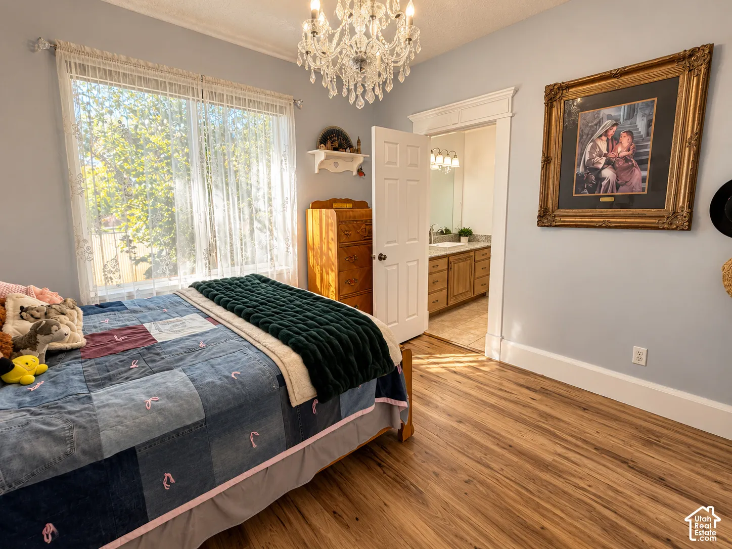 Spacious bedroom featuring hardwood flooring, a crystal chandelier, and abundant natural light from large windows